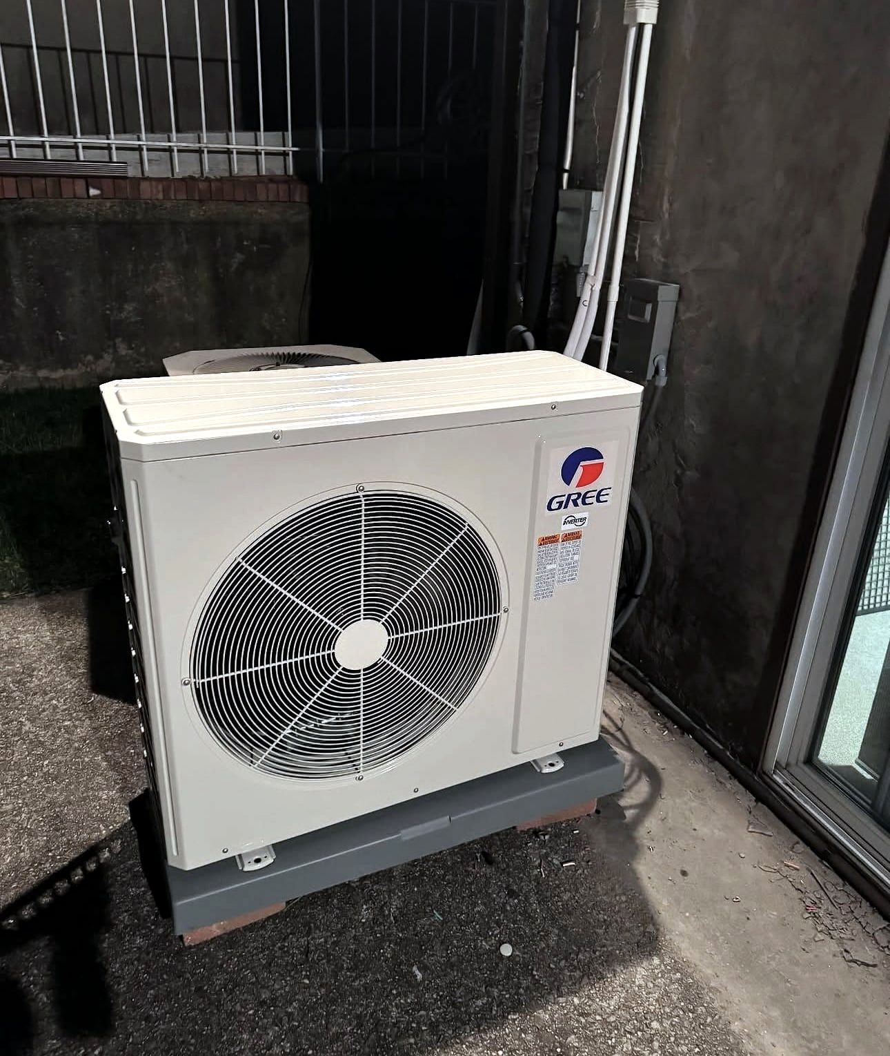 Gree outdoor condenser unit installed on a gray pad at night